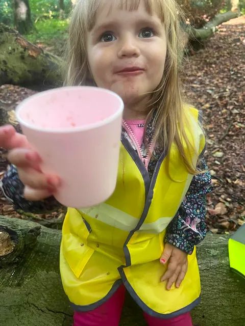 Young child in a high-visibility vest holding a cup outdoors