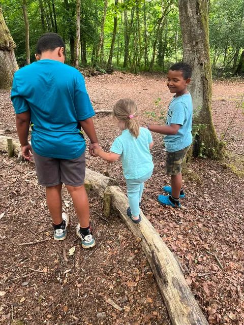 Children balancing on a fallen log in the forest with an adult