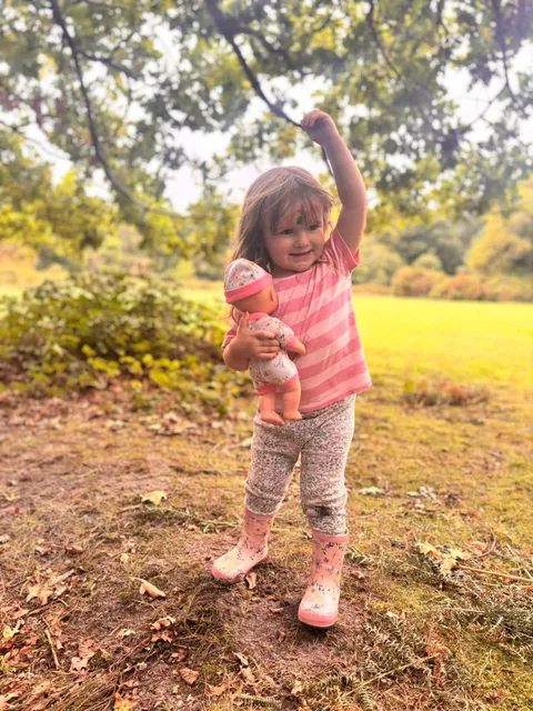 Young child holding a doll in a woodland clearing