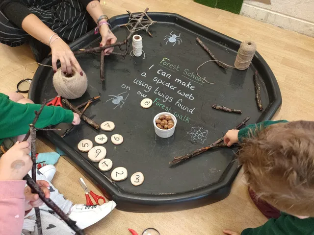 Children making a spider web from twigs on a Forest School activity tray