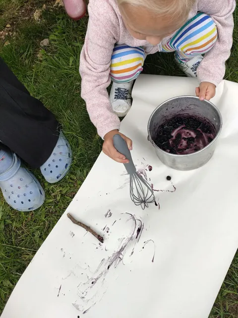 Toddler mixing foraged blackberry paint in a pan outdoors