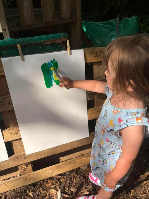 Young child painting at an easel outdoors