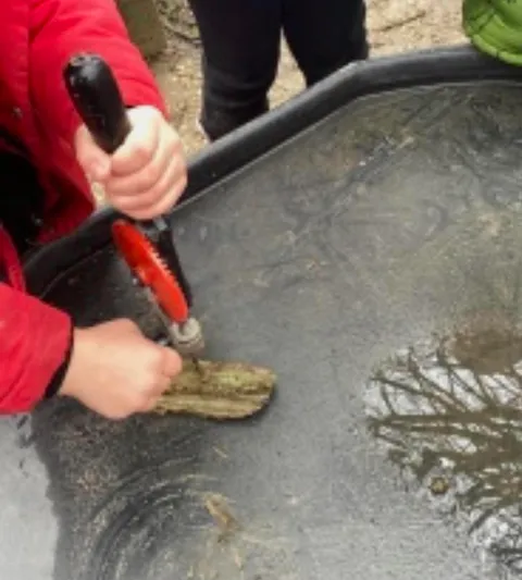 Child using a hand drill on wood at a water tray